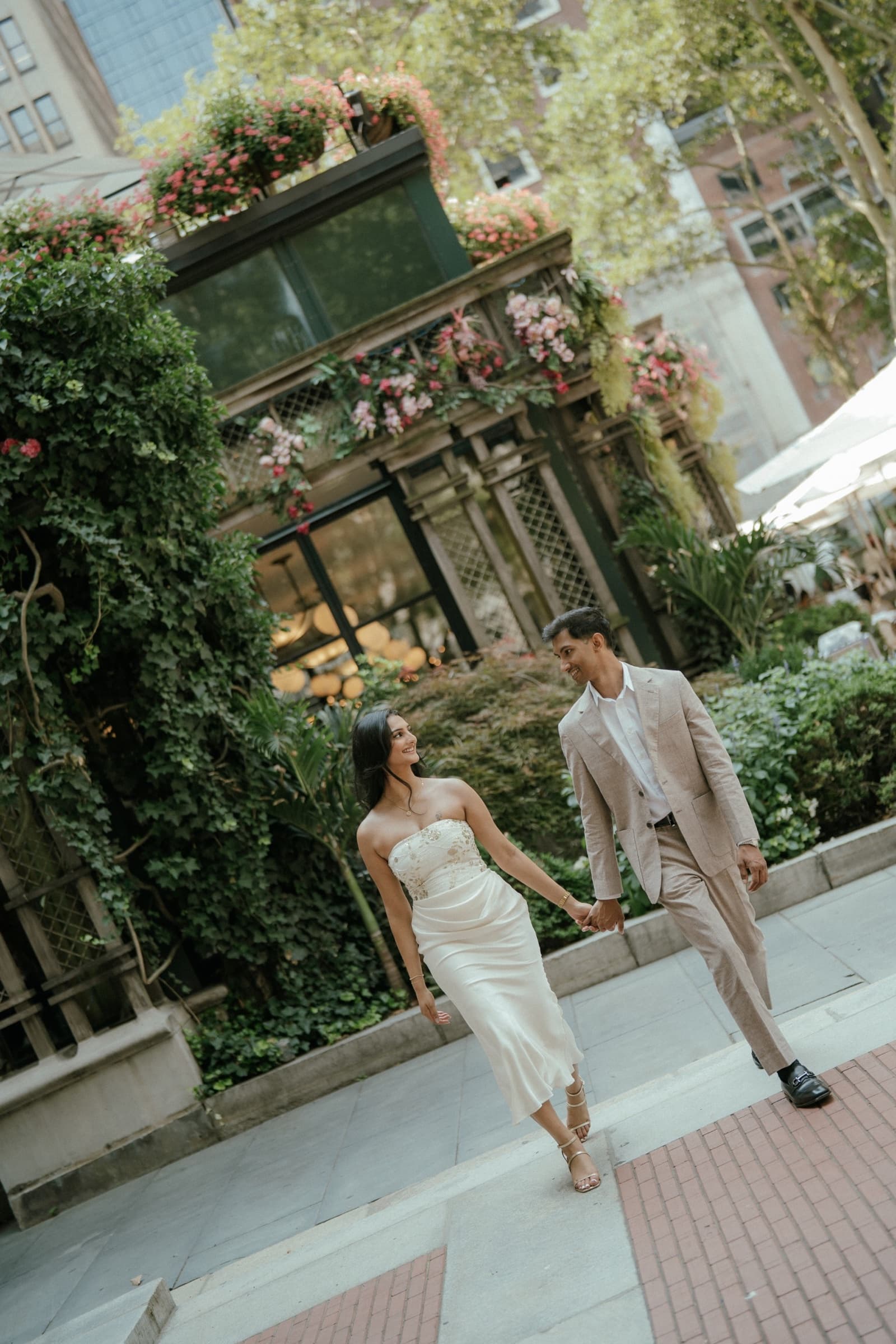 Ananya and Varun walking hand in hand through a garden courtyard