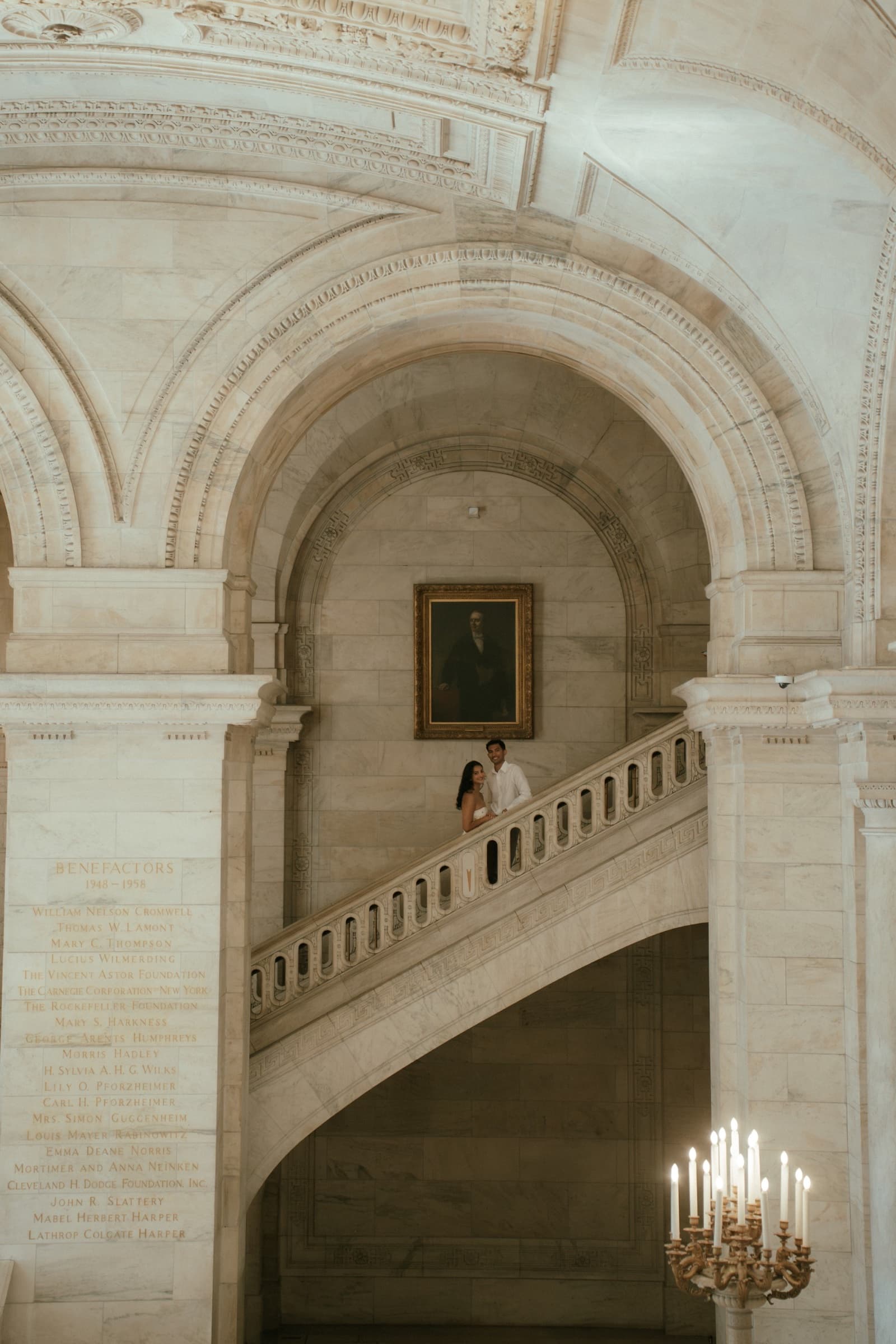 Ananya and Varun standing together on a grand marble staircase beneath vaulted arches